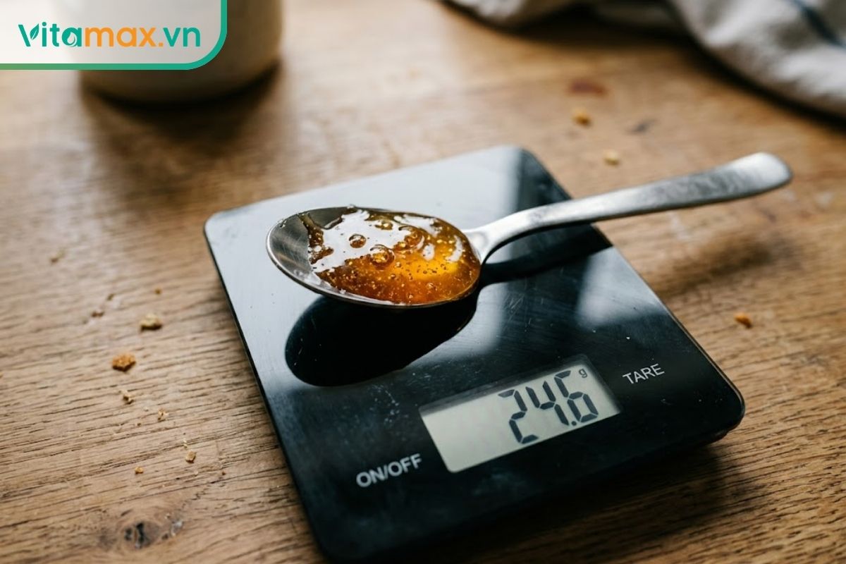 Một thìa cà phê chứa đầy mật ong được đặt gọn gàng trên chiếc cân điện tử nhà bếp, màn hình cân hiển thị những con số định lượng sắc nét.