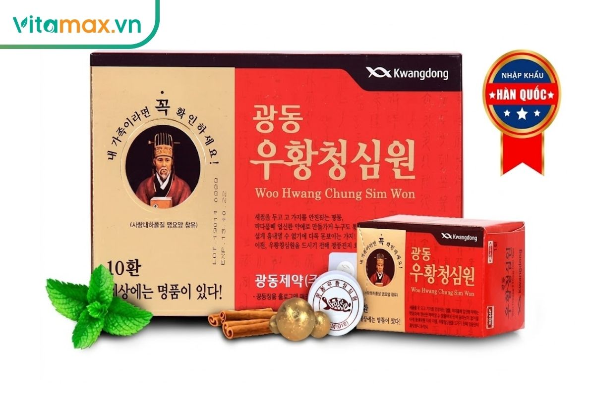 Hộp An Cung Ngưu Hoàng Hoàn Kwangdong màu đỏ kem cùng hộp nhỏ, viên hoàn bọc vàng và một số dược liệu trên nền trắng.