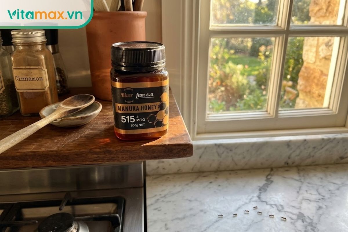 Hũ mật ong thủy tinh để trên kệ gần khu vực bếp nấu và cửa sổ, có ánh nắng ấm chiếu vào làm mật hơi loãng.