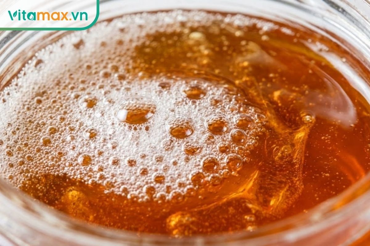 Ảnh chụp macro bề mặt mật ong với các bong bóng khí trắng nhỏ li ti, mịn màng, không có dấu hiệu nấm mốc.