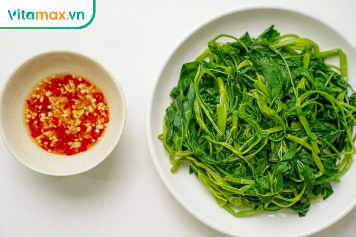 Cận cảnh một đĩa rau muống luộc xanh mướt, tươi ngon được bày trên bàn ăn gỗ, bên cạnh là một chén nước chấm nhỏ, minh họa cho cách chế biến đơn giản và lành mạnh.