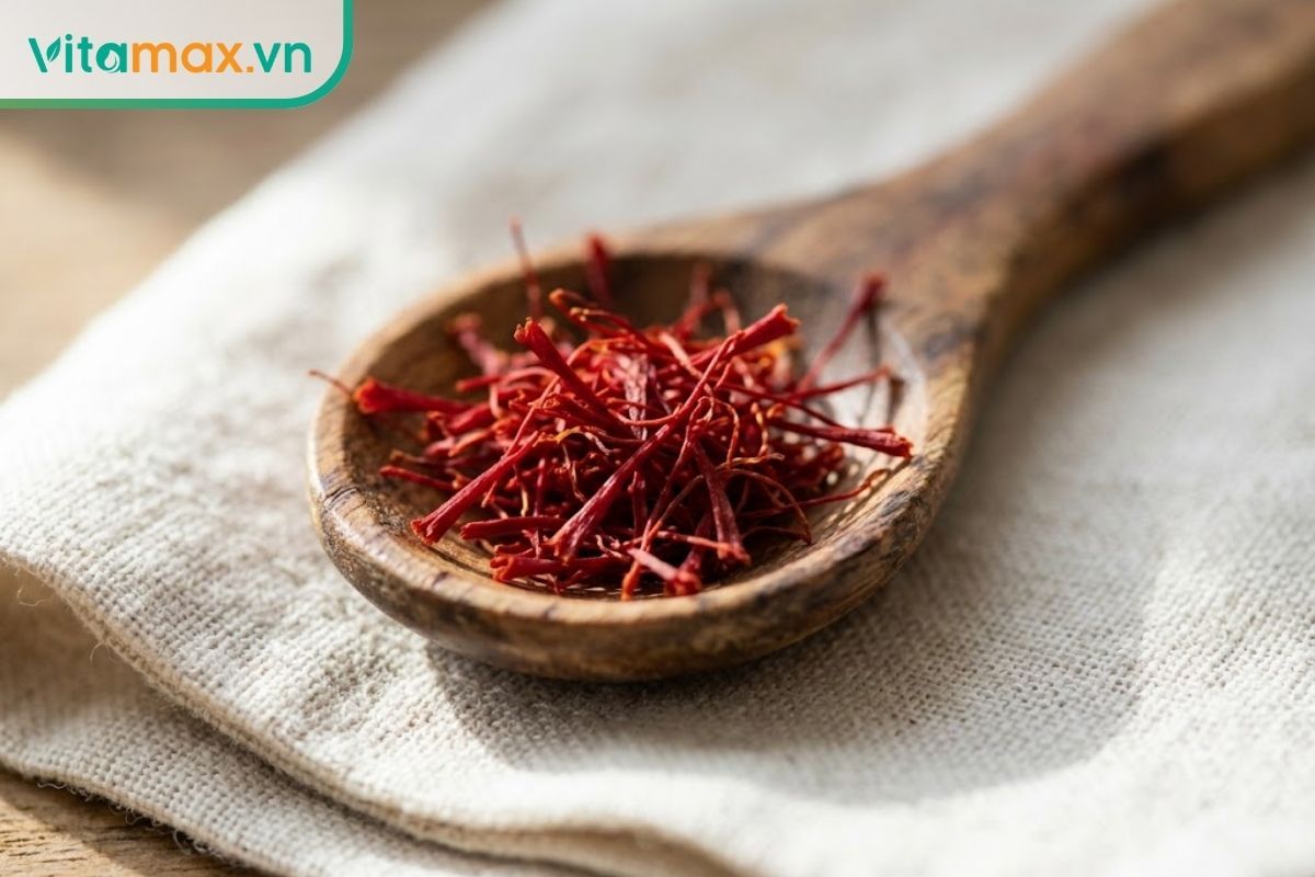 Cận cảnh những sợi nhụy hoa nghệ tây saffron chất lượng cao, khô ráo và có màu đỏ sẫm đồng đều, được đặt cẩn thận trong một chiếc muỗng gỗ nhỏ trên mặt bàn.
