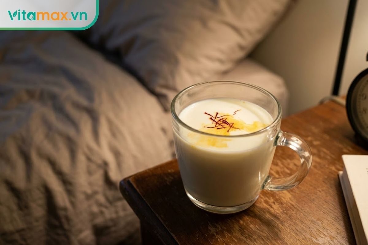 Ly sữa ấm ngâm những sợi nhụy hoa nghệ tây saffron đang chuyển sang màu vàng nhạt được đặt trên bàn cạnh giường ngủ.