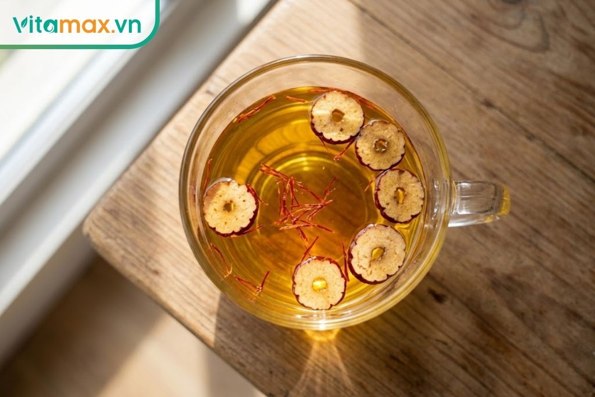 Một ly thủy tinh chứa trà saffron màu vàng ấm áp pha cùng vài lát táo đỏ sấy khô đặt trên bàn ăn.