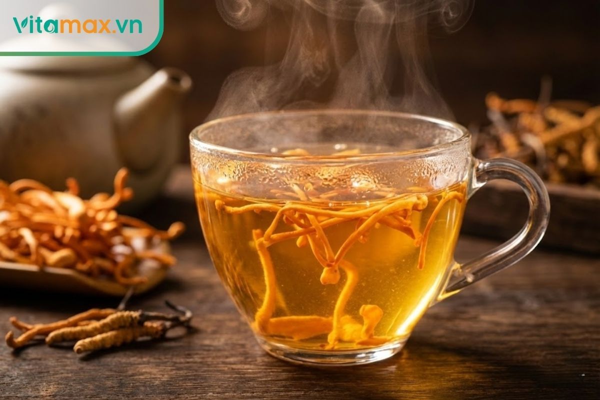 Cận cảnh ly trà đông trùng hạ thảo màu vàng óng với sợi nấm tươi ngon, khói bốc lên nhẹ nhàng.