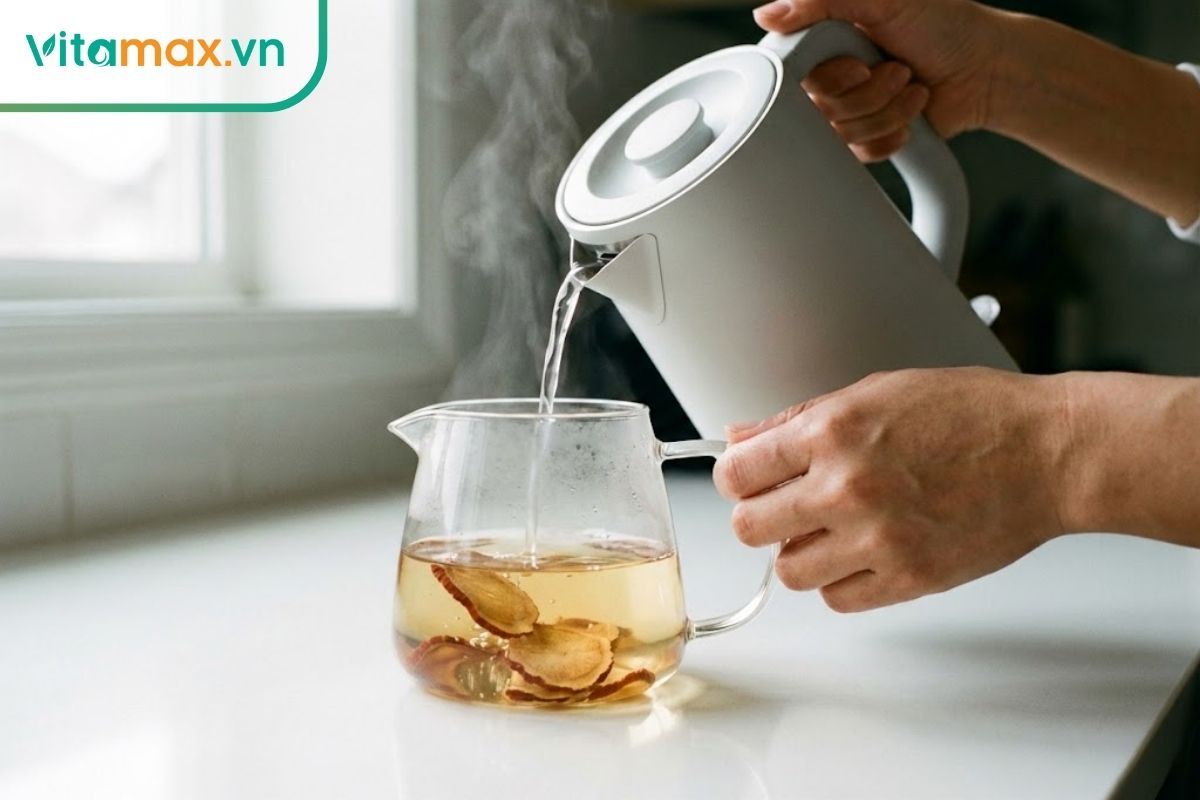 Đôi tay người phụ nữ đang rót nước nóng vào ấm trà thủy tinh chứa hồng sâm.