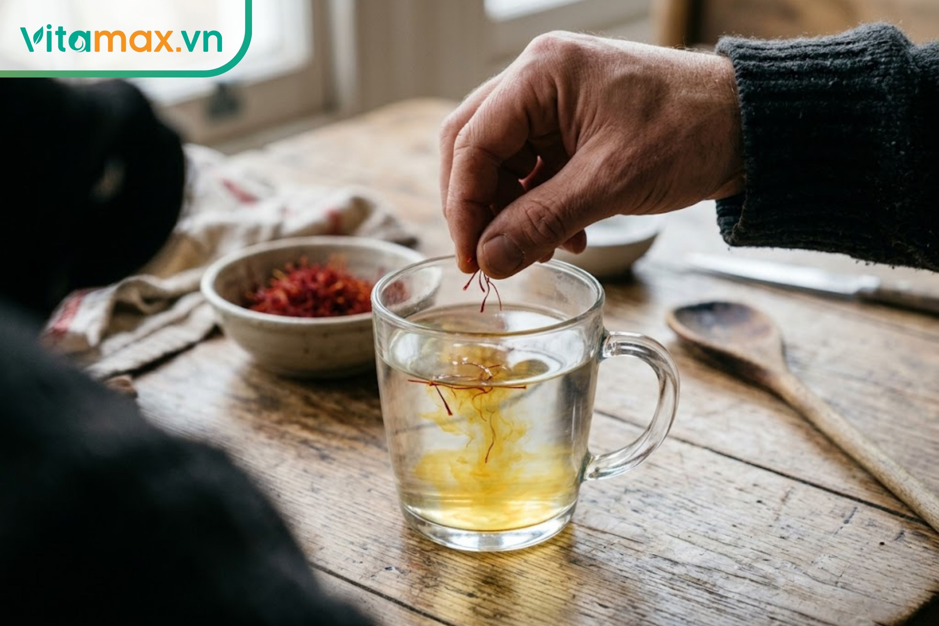 Tay người đàn ông đang thả nhẹ những sợi saffron đỏ nguyên chất vào cốc nước ấm để pha trà.