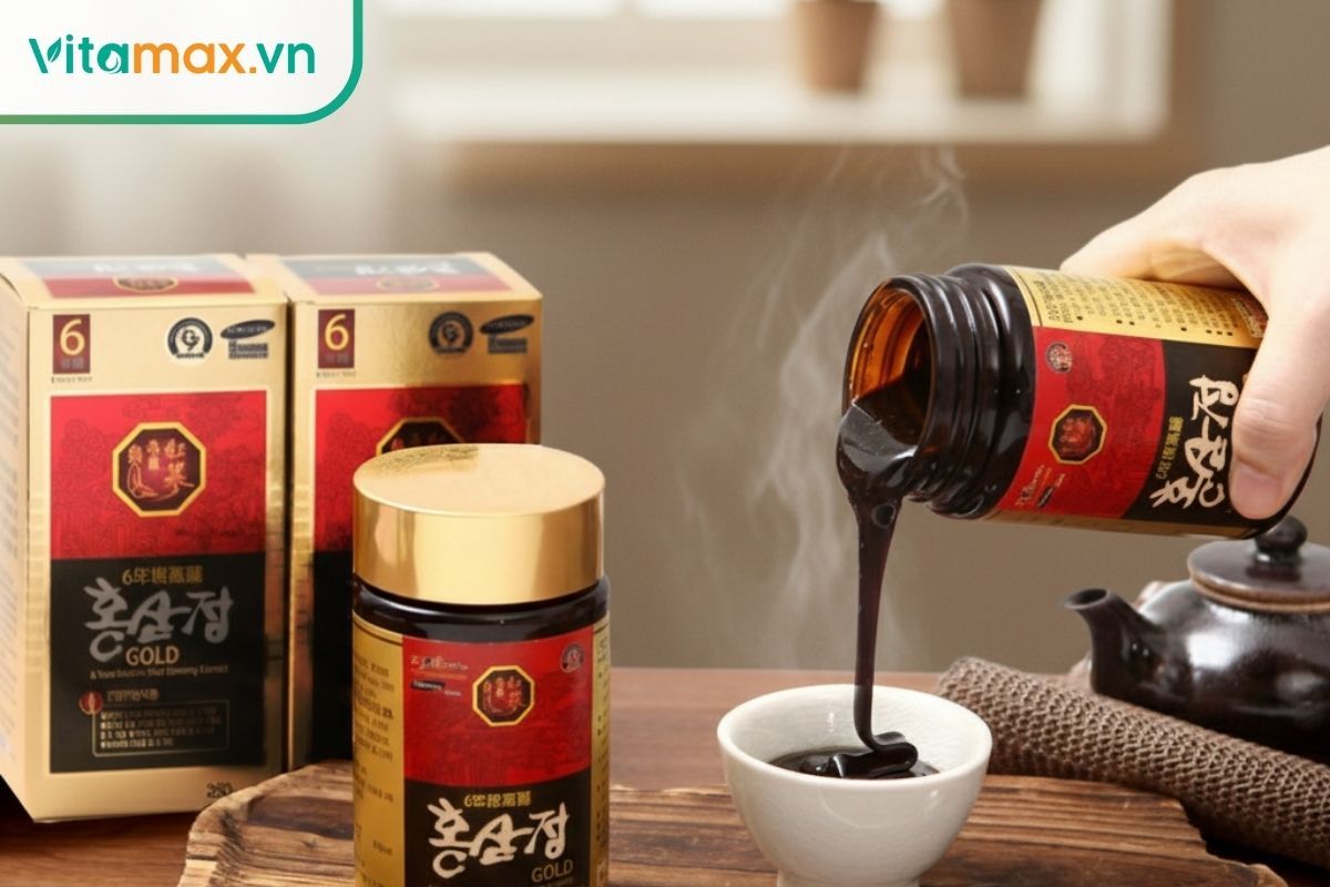  Cận cảnh một bàn tay đang rót cao hồng sâm Hàn Quốc 6 năm tuổi đặc sệt, màu nâu sẫm từ lọ thủy tinh nắp vàng vào một chiếc chén sứ trắng. Bên cạnh là hộp đựng sản phẩm và một ấm trà trên bàn gỗ.