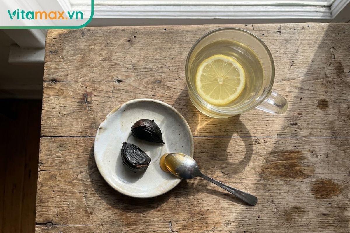 Vài tép tỏi đen cô đơn đã bóc vỏ đặt cạnh ly nước chanh mật ong ấm trên bàn ăn, một công thức biến thể có hương vị khá mạnh.