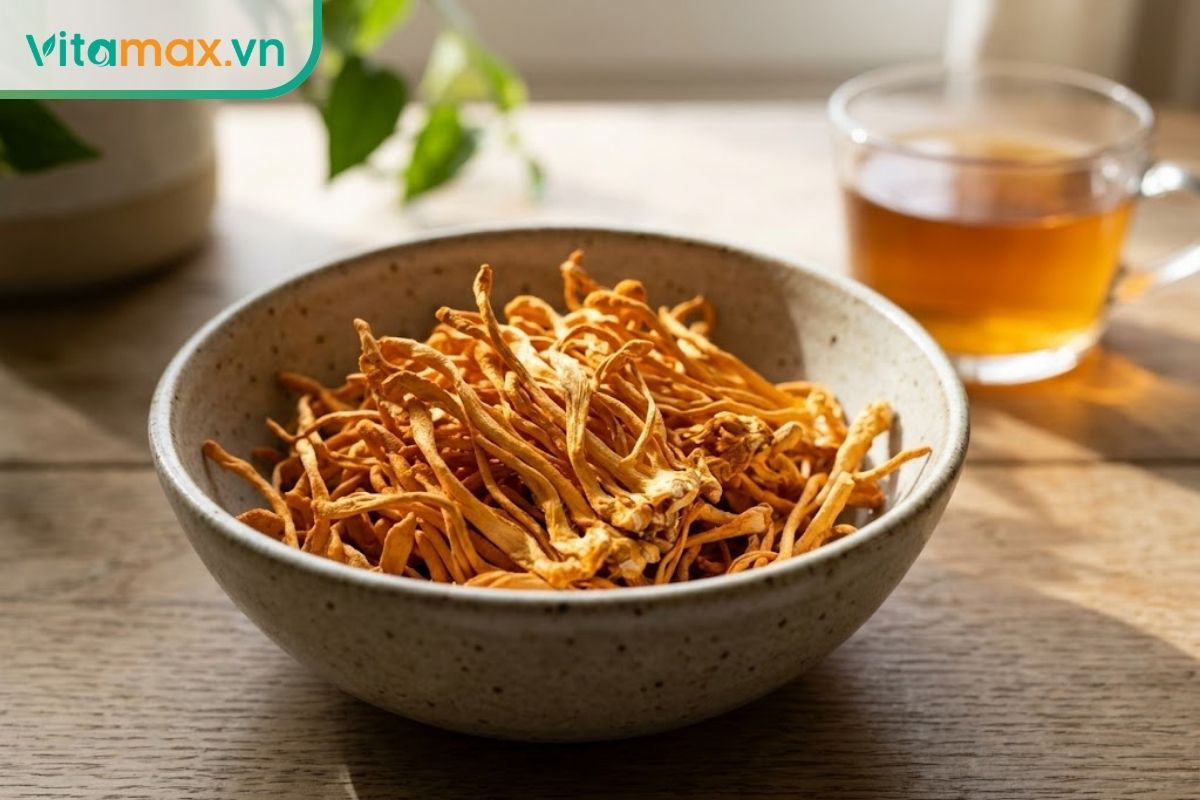 Những sợi nấm đông trùng hạ thảo sấy khô màu vàng cam đặt trên bát gốm, bối cảnh ánh sáng tự nhiên mộc mạc.