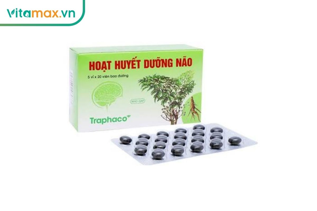 Hộp Hoạt Huyết Dưỡng Não Traphaco tông xanh lá đặt phía sau vỉ thuốc màu bạc chứa nhiều viên bao đường sẫm màu.