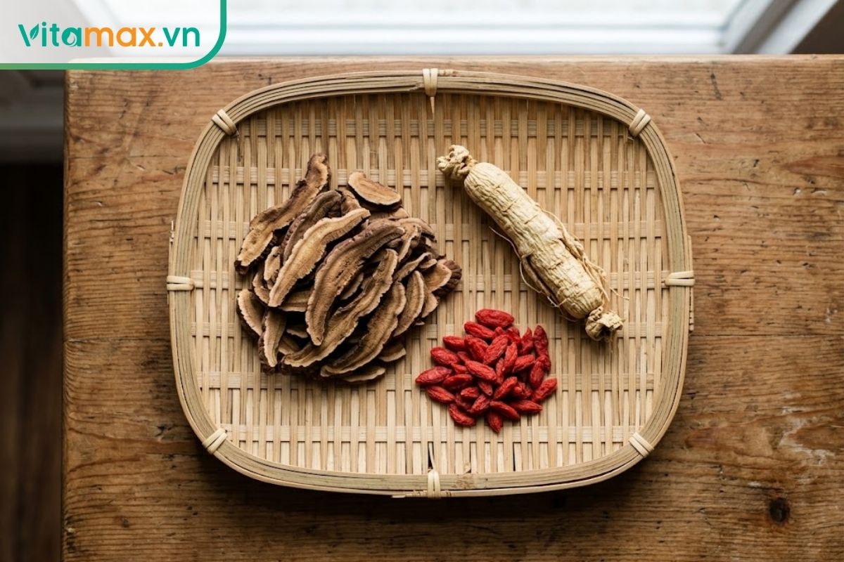 Các lát nấm linh chi, củ nhân sâm khô và một nắm hạt kỷ tử đỏ được bày biện gọn gàng trên một chiếc mẹt tre nhỏ, chuẩn bị để ngâm rượu.