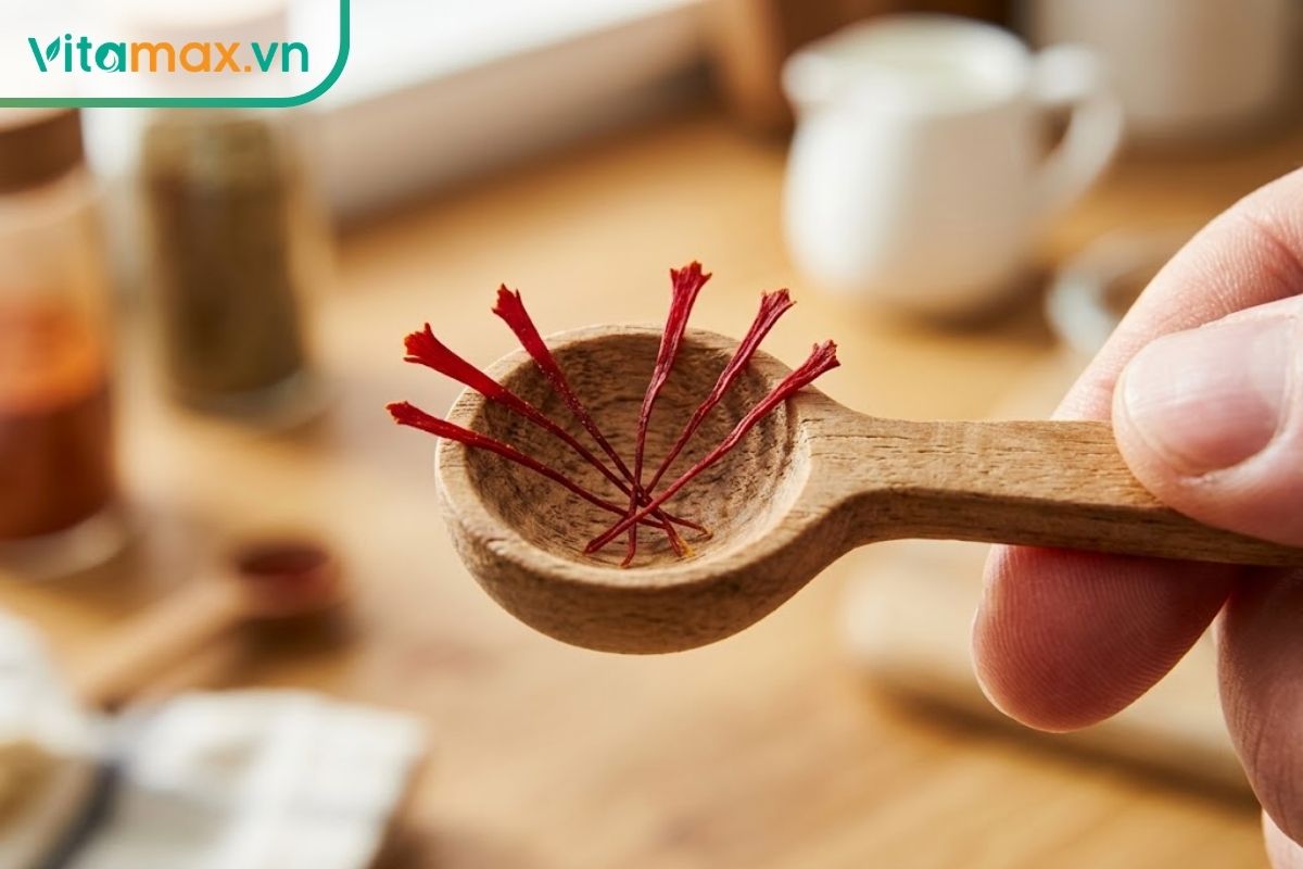 Cận cảnh 5 sợi nhụy hoa nghệ tây nguyên bản màu đỏ đậm nằm trên một chiếc thìa gỗ nhỏ gọn để chuẩn bị pha sữa.