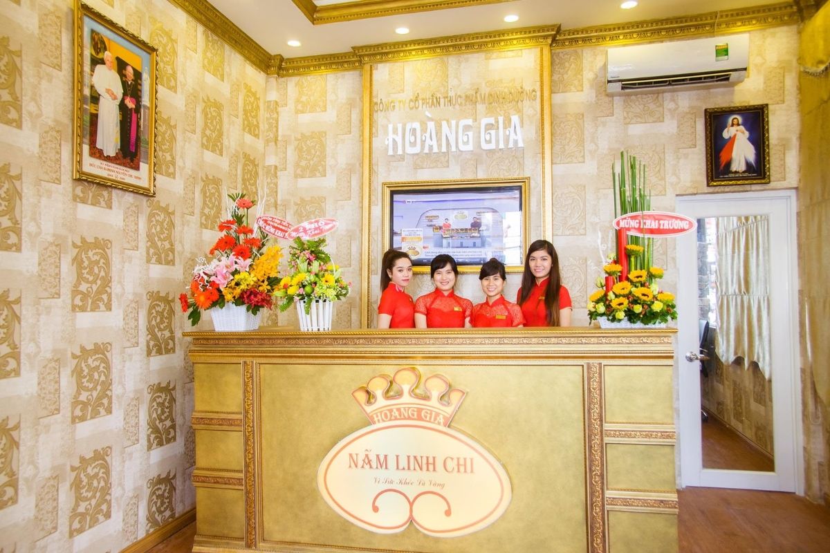 Quầy lễ tân showroom Linh Chi Hoàng Gia với nhân viên mặc áo đỏ và không gian trang trí màu vàng