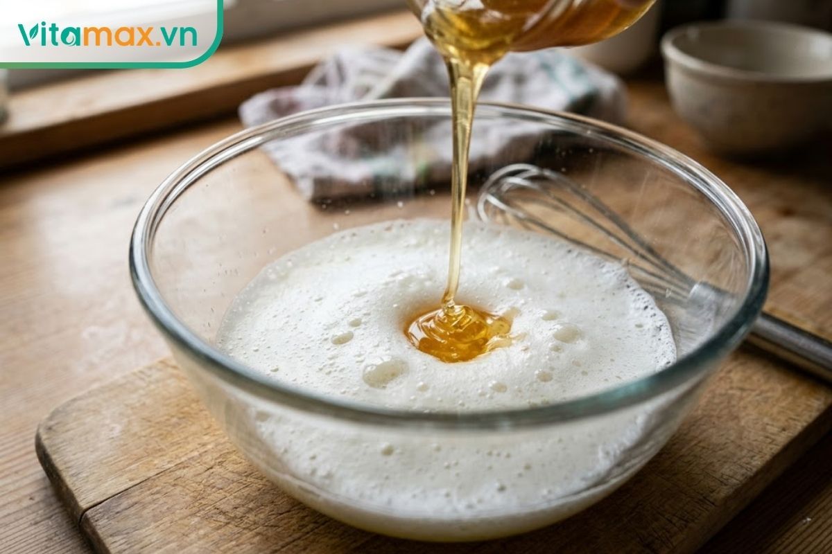 Cận cảnh bát thủy tinh đựng mặt nạ lòng trắng trứng đánh nổi bọt nhẹ trộn cùng mật ong thô nguyên chất.