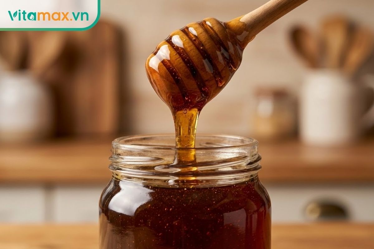 Hũ mật ong hoa Manuka có kết cấu đặc sệt, màu vàng nâu đậm và độ sánh cao đang chảy từ thìa gỗ.