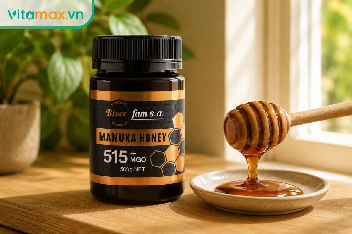 Lọ mật ong Manuka màu hổ phách sẫm đặt trên bàn bếp gỗ, kèm theo que lấy mật bằng gỗ đang nhỏ giọt mật ong đặc sánh.