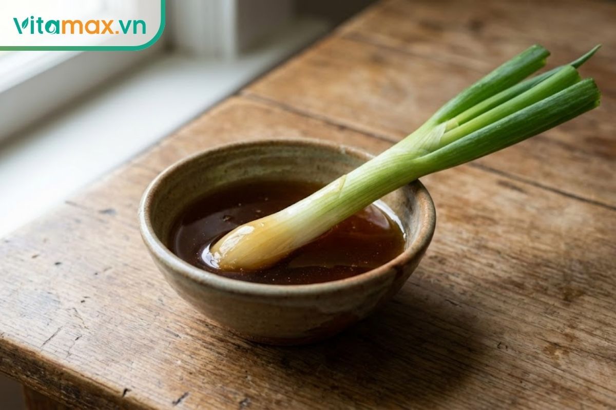 Cọng hành lá tươi được nhúng vào bát mật ong đặc sánh, minh họa mẹo thử dân gian.