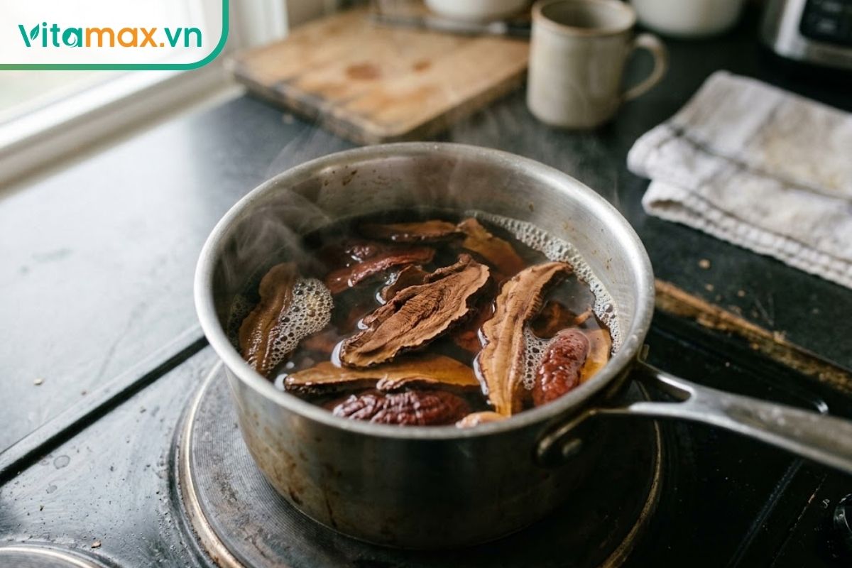 Nấm linh chi thái lát đang được nấu liu riu trong nồi inox, nước chuyển màu hổ phách trên bếp gia đình.