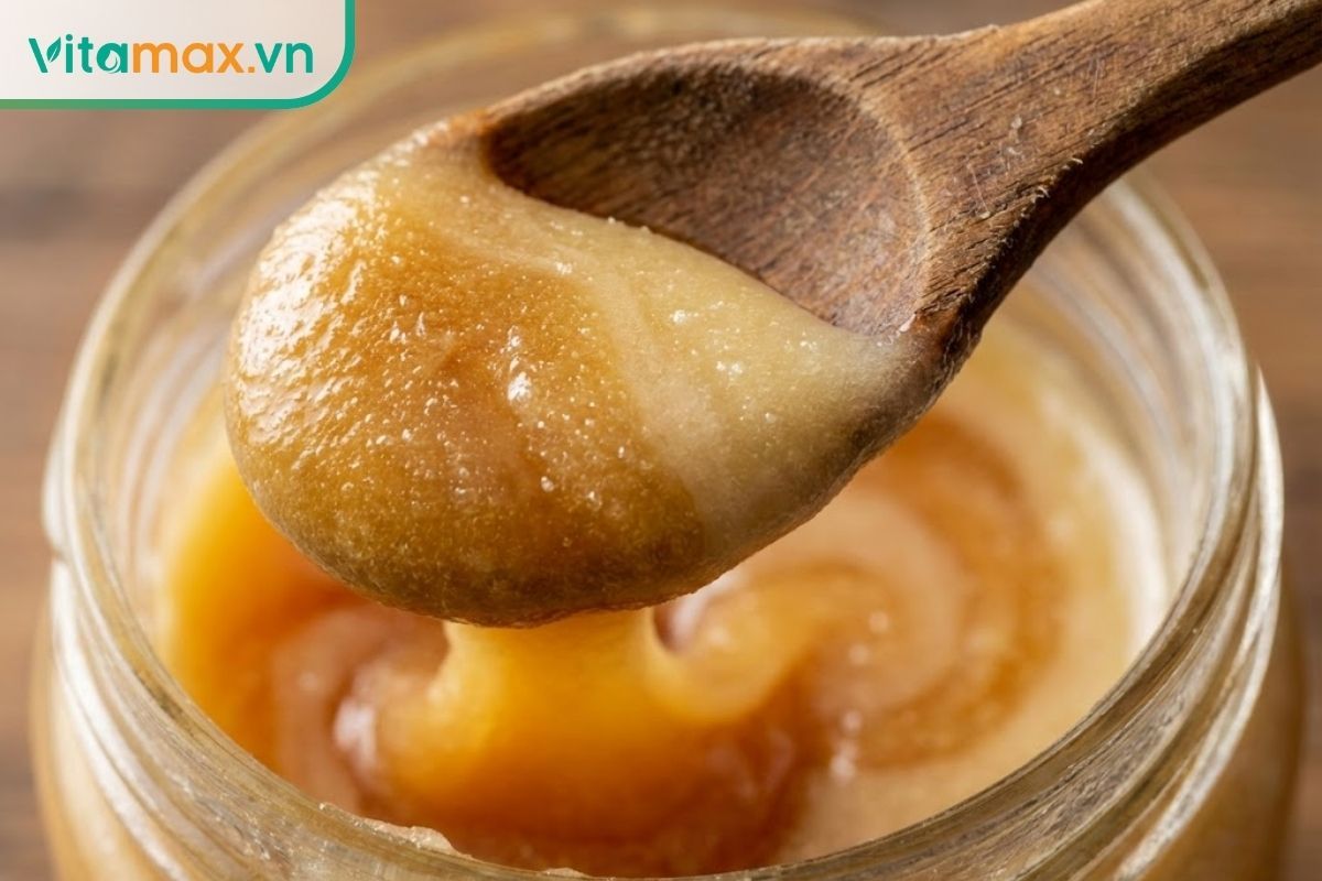 Cận cảnh thìa gỗ đang múc lớp mật ong đóng đường mịn màng, màu vàng óng, không bị tách lớp.