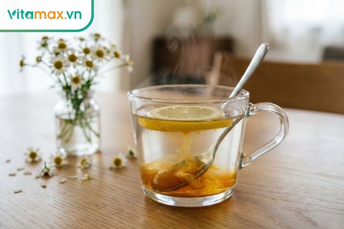 Ly nước ấm pha mật ong Manuka và lát chanh tươi trên bàn gỗ, hơi nước bốc lên nhẹ.