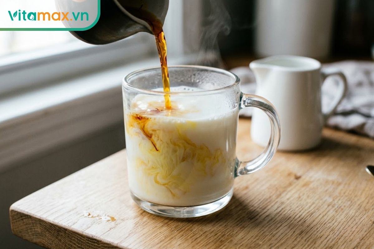 Dòng nước nhụy hoa nghệ tây màu hổ phách đậm đặc đang được rót vào một ly thủy tinh chứa sữa trắng ấm, tạo ra những vệt xoáy màu vàng nhạt béo ngậy.