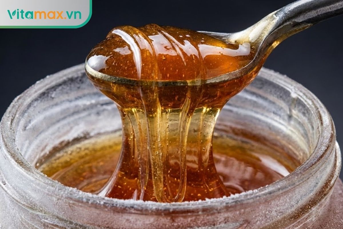 Cận cảnh thìa inox đang múc một khối mật ong lạnh dẻo quánh như mạch nha, không bị đông cứng thành đá.