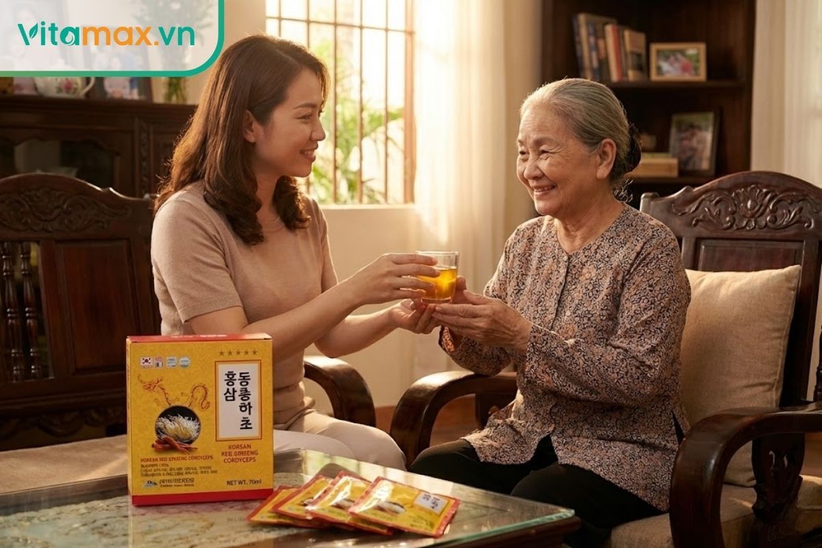 Con gái đang ân cần mời mẹ uống nước đông trùng hạ thảo, trên bàn là hộp quà màu đỏ vàng.