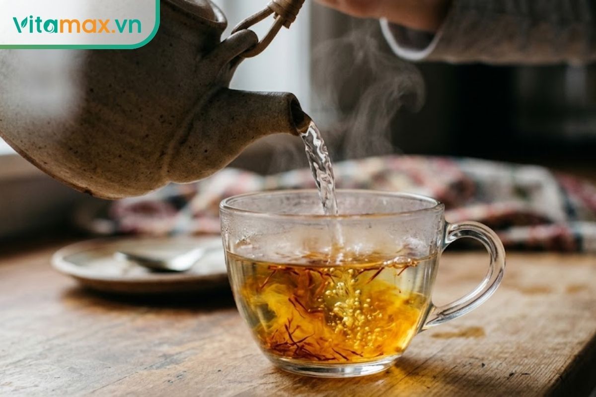 Cận cảnh dòng nước nóng được rót từ ấm vào tách thủy tinh chứa sẵn sợi saffron, làm bung tỏa màu vàng óng.