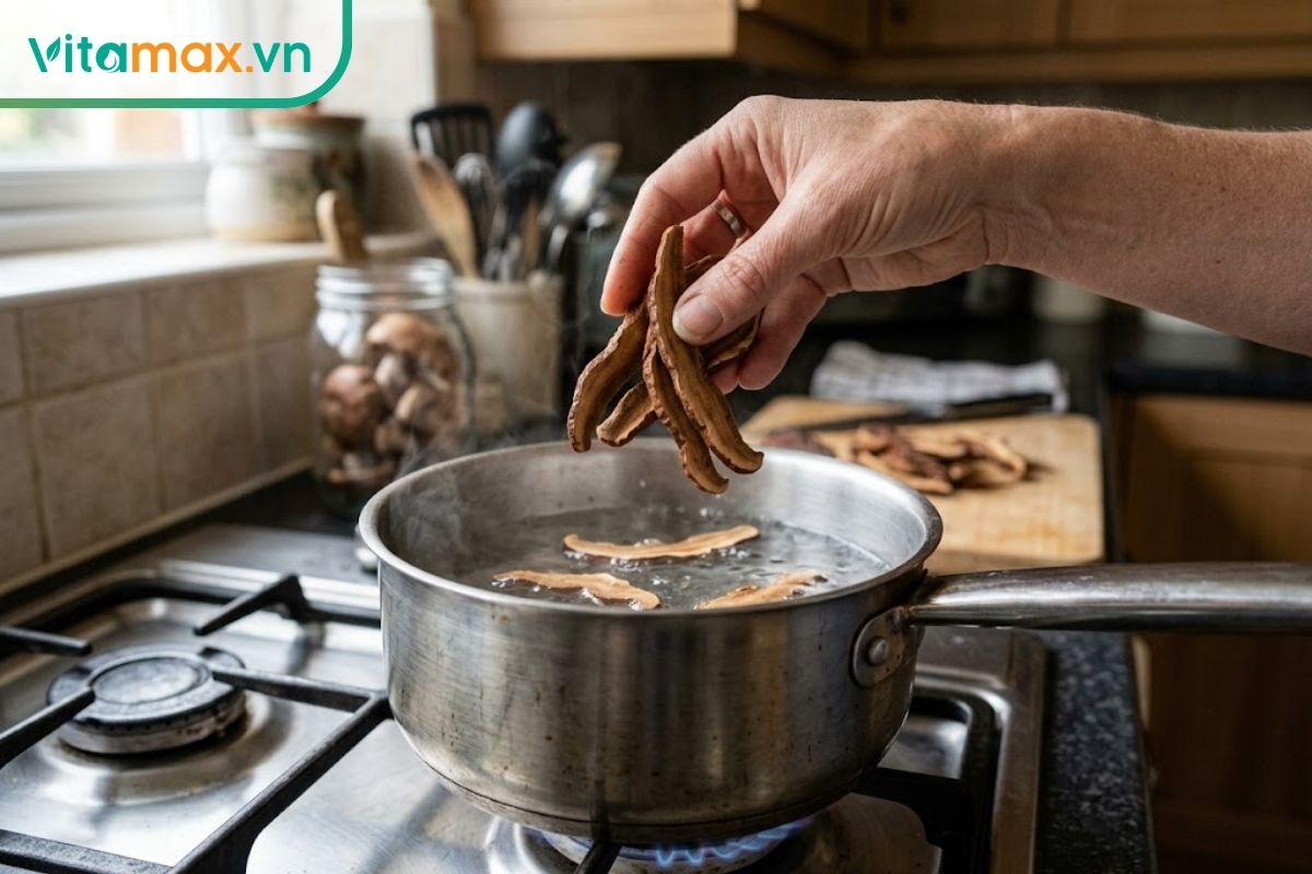 Bàn tay cho nấm linh chi thái lát vào nồi nước trên bếp để sắc, minh họa bước chuẩn bị nước linh chi uống tại nhà.
