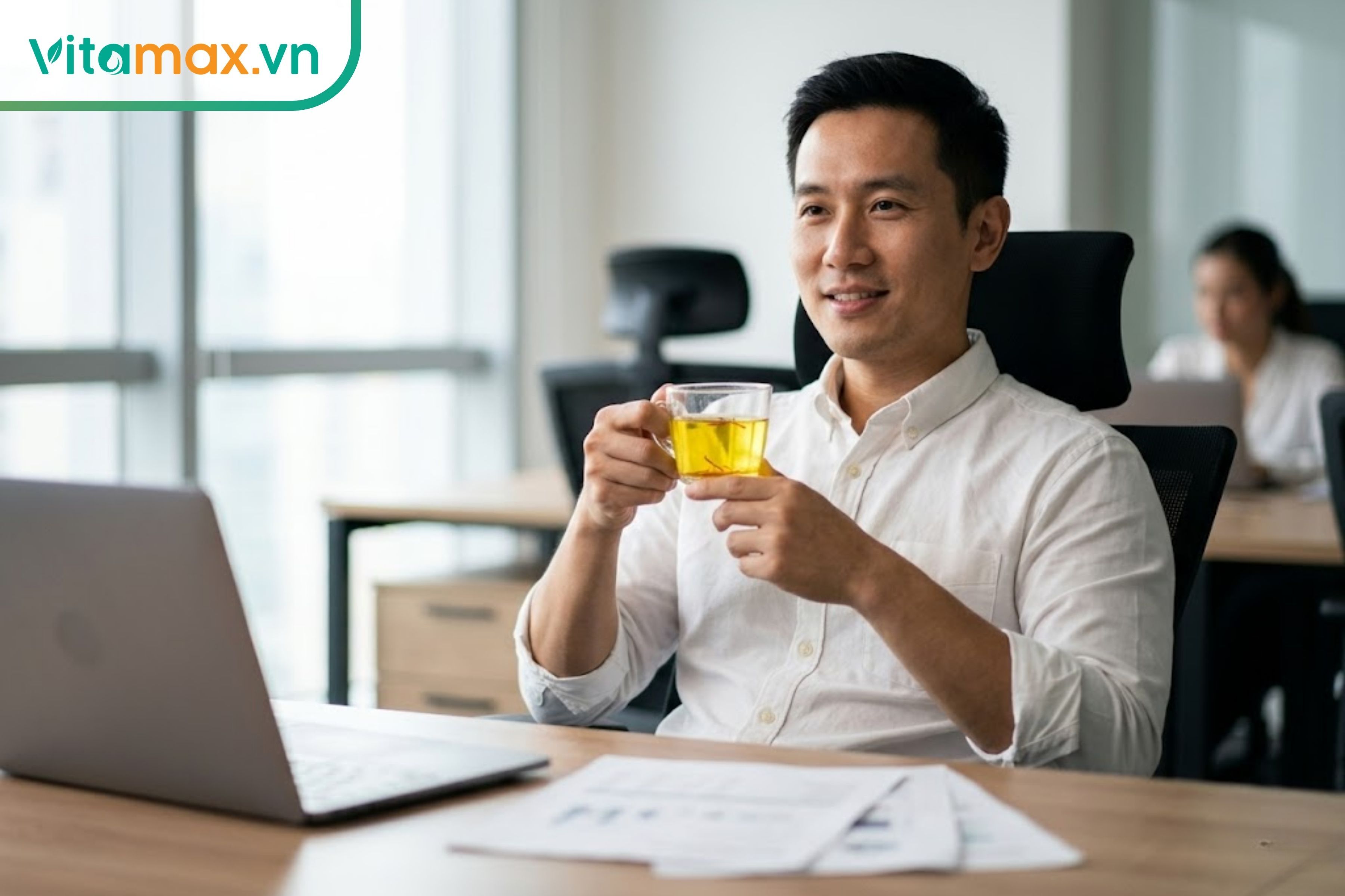 Nhân viên văn phòng nam giới đang thư giãn, giảm stress tại bàn làm việc với một ly trà saffron ấm.