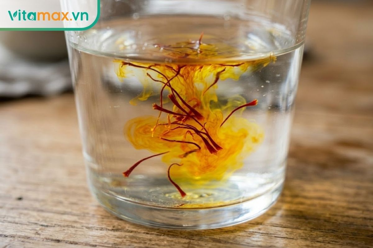 Cận cảnh những sợi nhụy hoa nghệ tây saffron đỏ thẫm đang hòa tan ra màu vàng óng trong ly nước ấm giúp hỗ trợ sức khỏe sinh lý.