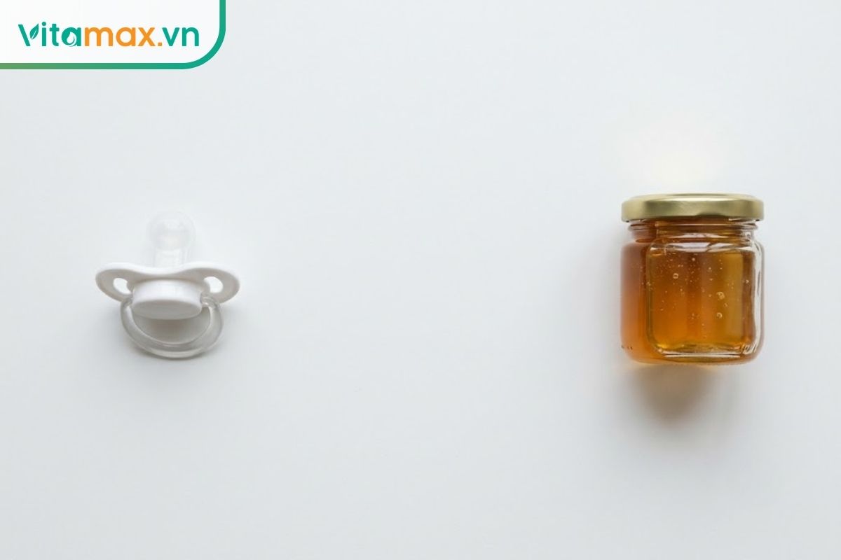 Một hũ thủy tinh chứa mật ong nguyên chất màu hổ phách tuyệt đẹp với nhãn mác thiết kế tối giản, đặt trên thớt gỗ cùng vài lát chanh tươi trong căn bếp ngập nắng.