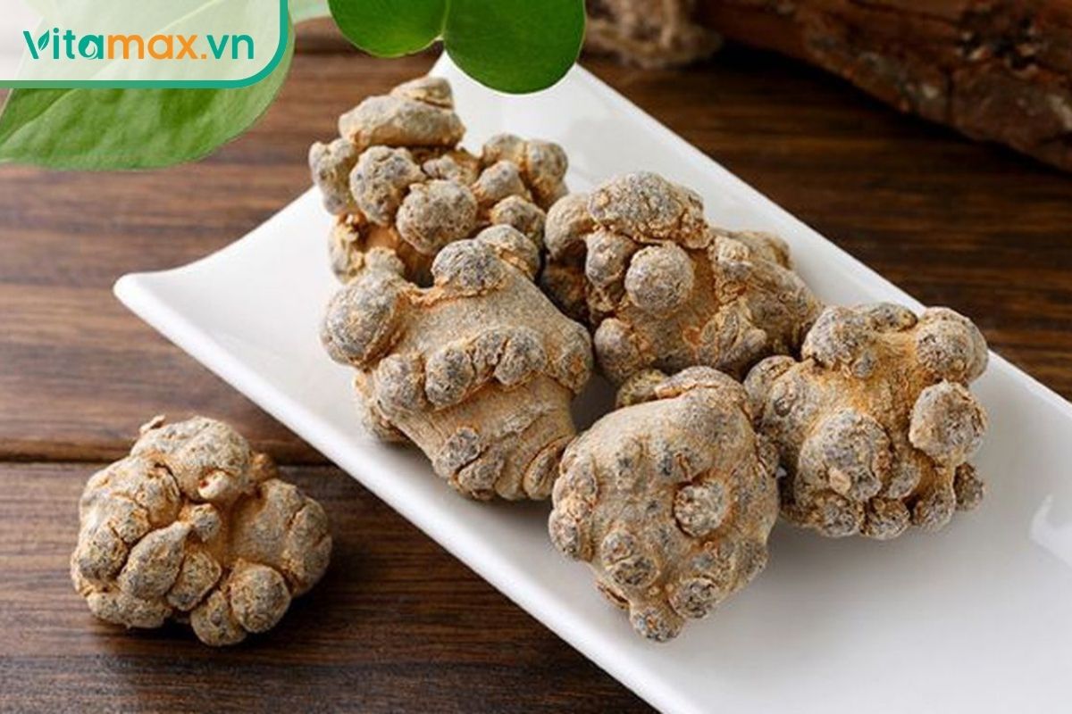 Các củ tam thất khô màu nâu xám có nhiều u nhỏ trên bề mặt, được sắp xếp trên đĩa trắng đặt trên nền gỗ.