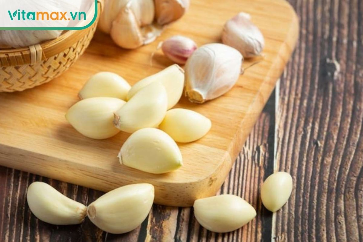Các tép tỏi tươi đã bóc vỏ và củ tỏi đặt trên thớt gỗ.