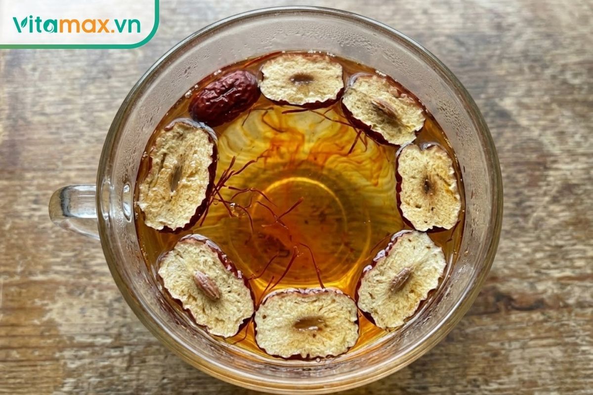Cận cảnh những lát táo đỏ sấy khô và sợi saffron thật đang ngâm trong nước nóng, tiết ra màu vàng cam óng ánh bắt mắt.