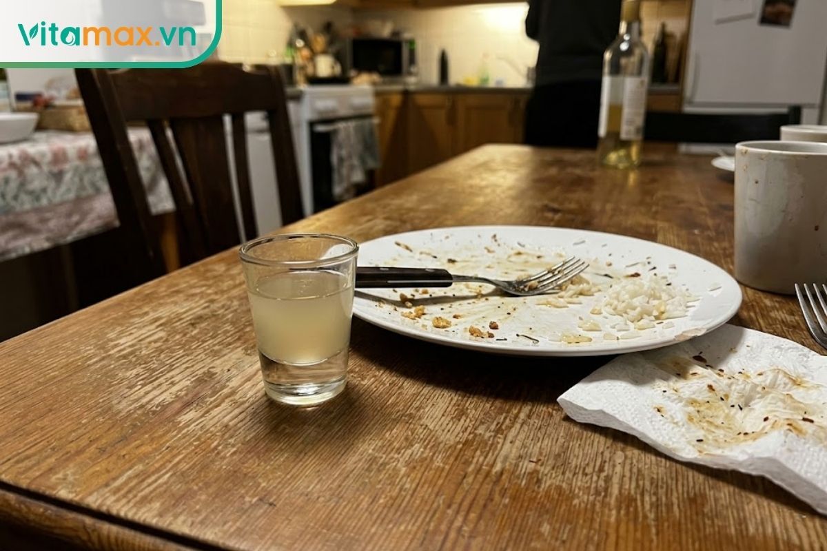 Một ly nhỏ chứa rượu tỏi mật ong đặt cạnh đĩa thức ăn đã dùng xong để hỗ trợ tiêu hóa.